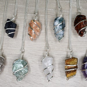 Puede incluir: Diez collares de cadena de plata con diferentes colgantes de cristal de colores envueltos en alambre de plata. Los cristales incluyen negro, naranja, verde, blanco, marrón y morado.