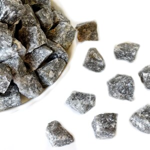 May include: A pile of small, gray, irregularly shaped stones in a white bowl. Some stones are scattered on a white surface.