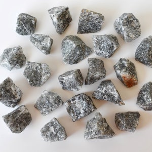 May include: A collection of 20 grey and black tumbled stones. The stones are various sizes and shapes, with some having a slightly rough texture.