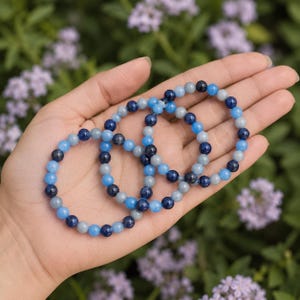 May include: Three circular bracelets made of polished spherical beads in alternating shades of dark navy blue, medium sky blue, and light grey. The beads are strung on an elastic cord, creating a flexible and lightweight jewelry accessory.