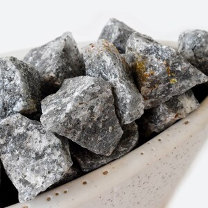 May include: A close-up of a bowl filled with gray and white stones. The stones are smooth and have a natural, rough texture.