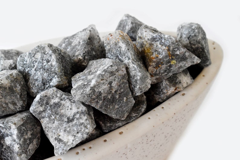 May include: A close-up of a bowl filled with gray and white stones. The stones are smooth and have a natural, rough texture.