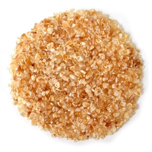 May include: A close-up of a pile of small, translucent, amber-colored crystals. The crystals are scattered on a white surface.