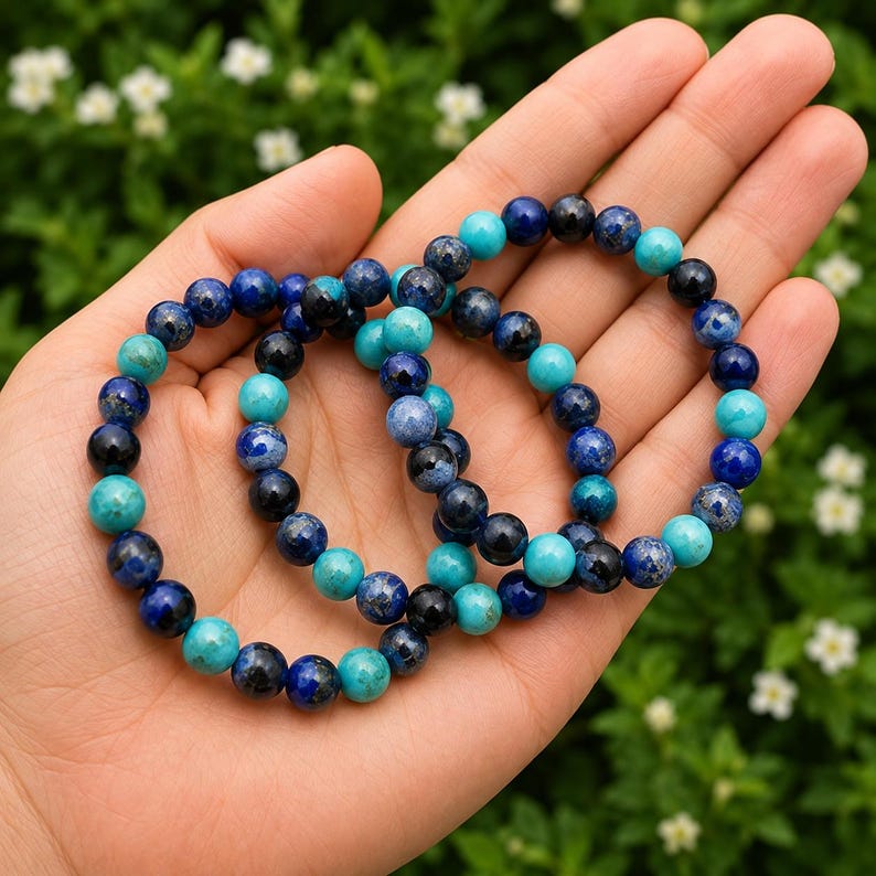 May include: Two stretch bracelets composed of round beads in varying shades of deep navy blue, royal blue, and bright turquoise. The beads feature natural mottled patterns and smooth, polished surfaces, arranged in a repeating color sequence.
