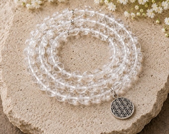May include: A multi-strand bracelet composed of clear, spherical beads arranged in a circular pattern. The bracelet features small silver-toned metal spacers and a round silver-toned pendant engraved with a geometric flower of life pattern.
