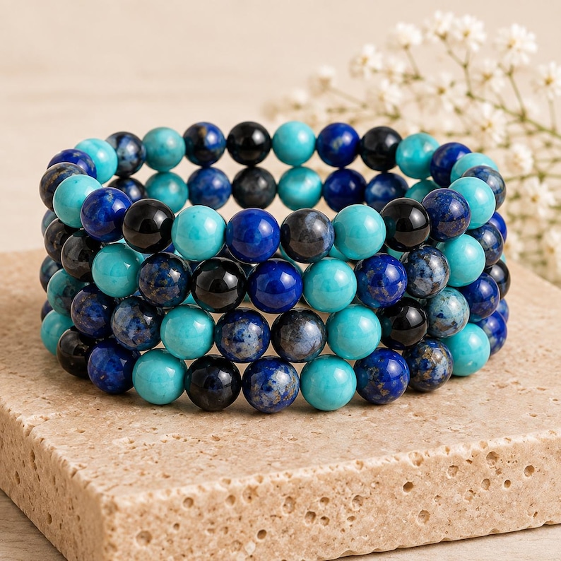 May include: A multi-strand beaded bracelet featuring a repeating pattern of polished spherical beads in shades of turquoise, deep royal blue, and glossy black. The beads are arranged in a circular formation, creating a dense, layered appearance.