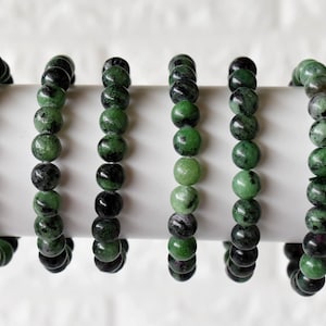 May include: Six green and black gemstone bracelets with round beads. The bracelets are stacked on a white surface.