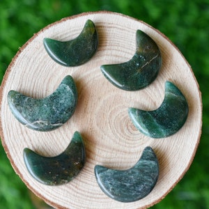 May include: Six green and brown crescent moon shaped polished stones on a wooden surface.