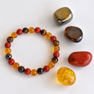 Pode incluir: Um bracelete feito com contas vermelhas, amarelas e marrons. O bracelete &eacute; rodeado por pedras soltas das mesmas cores.