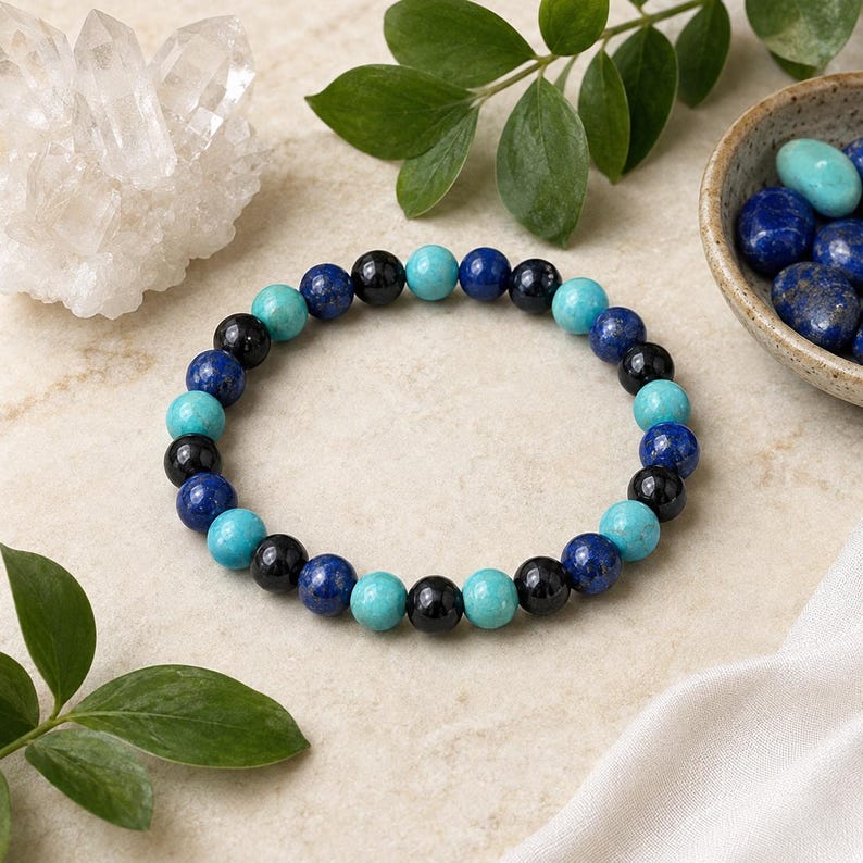 May include: A beaded bracelet featuring a repeating pattern of round polished beads in shades of turquoise blue, deep royal blue, and glossy black. The beads are strung on an elastic cord, creating a circular shape with a smooth, uniform texture.
