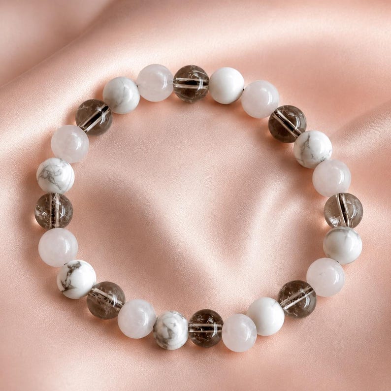 Puede incluir: Una pulsera circular de cuentas con cuentas redondas alternas en blanco s&oacute;lido, blanco y gris jaspeado, y marr&oacute;n oscuro transl&uacute;cido con inclusiones internas visibles. Las cuentas est&aacute;n ensartadas en un patr&oacute;n repetitivo formando un bucle.