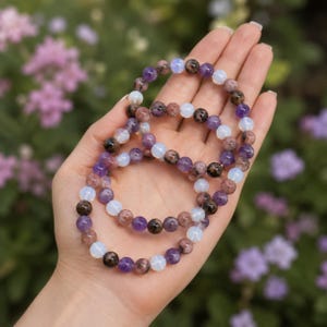 May include: Three elastic bracelets made of round beads in shades of purple, translucent white, and speckled brown. The beads are arranged in a repeating pattern, creating a colorful and textured look for these circular pieces of jewelry.
