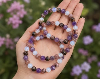 May include: Three elastic bracelets made of round beads in shades of purple, translucent white, and speckled brown. The beads are arranged in a repeating pattern, creating a colorful and textured look for these circular pieces of jewelry.