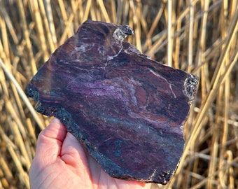 Könnte beinhalten: Ein großes, flaches Stück violett-schwarzen Bänderung-Agates mit einer rauen, natürlichen Kante. Der Achat hat ein wirbelndes Muster aus Violett, Schwarz und Weiß.