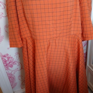 May include: Orange and black checkered dress with a sweetheart neckline and short sleeves. The dress has a flared skirt and is made of a lightweight fabric.