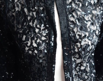 May include: A black sequined cropped jacket with a lace overlay. The jacket has a front closure with a single button.