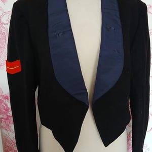 Peut inclure: Une veste de cérémonie noire et bleue avec une bande rouge sur la manche. La veste a un col châle et est taillée pour une coupe ajustée.
