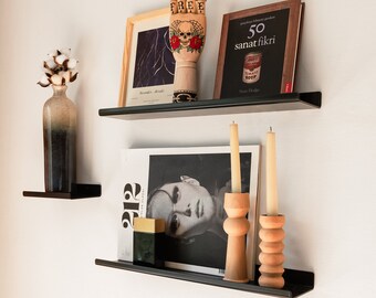 May include: Two black metal shelves with a wooden hand sculpture, a book titled "50 sanat fikri", a magazine, and two wooden candle holders with candles.