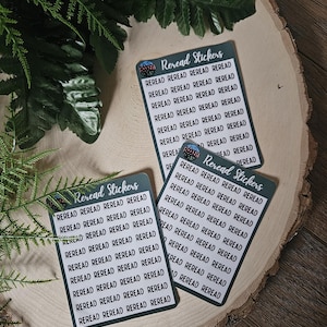 May include: Three sheets of stickers with the word "REREAD" repeated multiple times on each sheet. The stickers are on a light brown wooden surface.