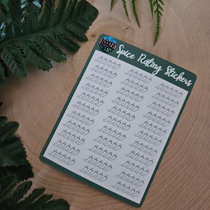 May include: A sheet of green sticker paper with white pepper stickers. The stickers are in the shape of peppers and are arranged in rows. The text "Spice Rating Stickers" is printed on the sheet.