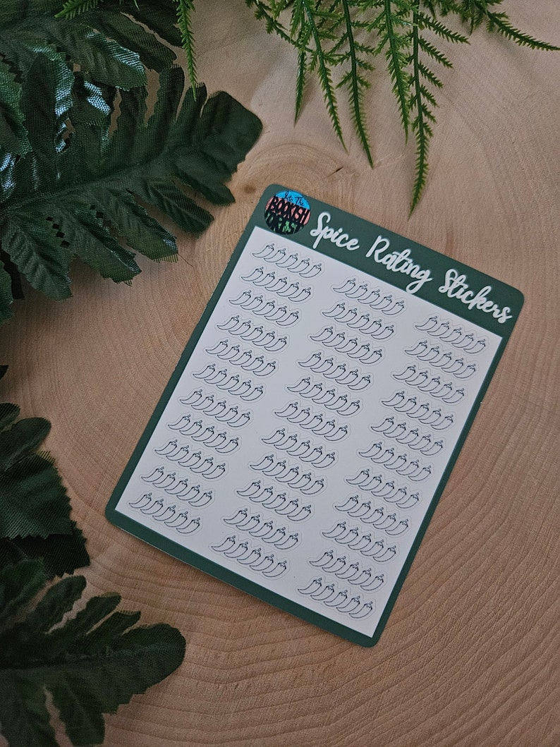 May include: A sheet of green sticker paper with white pepper stickers. The stickers are in the shape of peppers and are arranged in rows. The text "Spice Rating Stickers" is printed on the sheet.