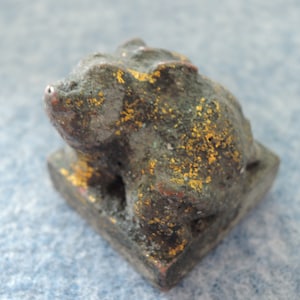 May include: A small, gray, ceramic frog figurine with gold accents. The frog is sitting on a square base.