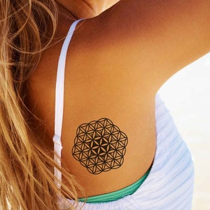 May include: A woman with long blonde hair is smiling and looking over her shoulder. She has a temporary tattoo of a black geometric design on her shoulder.