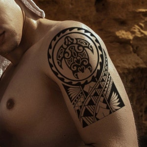 May include: A man with a white towel around his head and a black tribal tattoo on his upper arm. The tattoo features a turtle design.