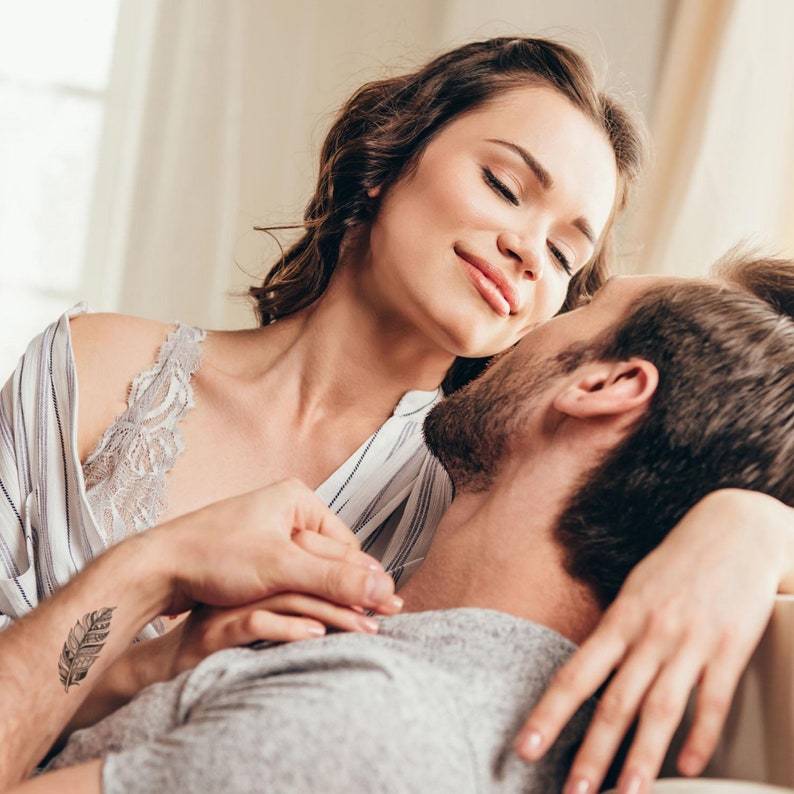 May include: A couple embracing, with the woman's arm around the man's neck. She has a small feather tattoo on her wrist.