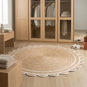 May include: A round, natural fiber rug with a scalloped edge and a white border. The rug is made of woven jute and has a concentric circular pattern. The rug is placed on a light-colored wooden floor.