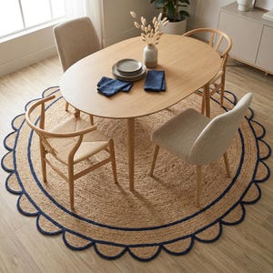 May include: A dining room scene featuring a light wood oval table set with plates and napkins. Four chairs surround the table, set on a round jute rug with a navy blue scalloped border. A vase with dried flowers sits on the table.