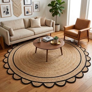 May include: A round jute rug with a scalloped black border. The rug is centered in a living room with a beige sofa, brown armchair, and a wooden coffee table. The rug's natural tones complement the room's neutral color scheme.