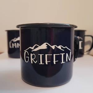 May include: A dark blue enamel mug with a white mountain range design and the name "GRIFFIN" printed below.