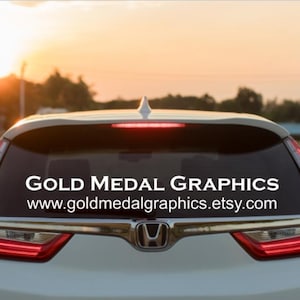 This is a picture of a car with custom lettering on the back window that identifies the business name and website of Gold Medal Graphics.