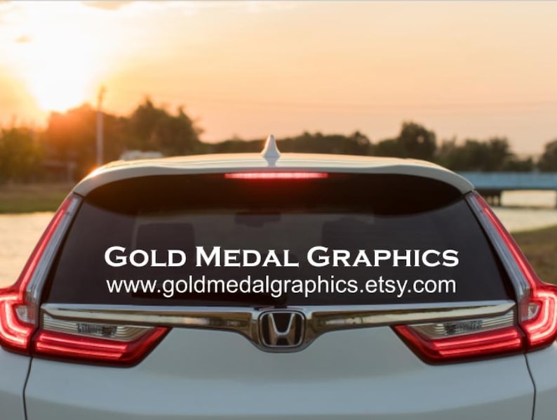 This is a picture of a car with custom lettering on the back window that identifies the business name and website of Gold Medal Graphics.