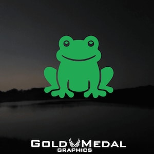 Op de afbeelding: Afbeelding van een groene, lachende kikker op een donkere achtergrond met een vage landschap. De tekst "GOLD MEDAL GRAPHICS" staat in het wit onderaan.
