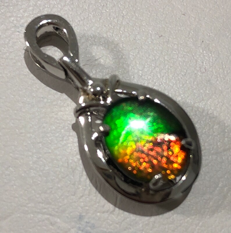 May include: A silver pendant with a teardrop-shaped iridescent gemstone. The gemstone has a green, orange, and red color.