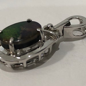 May include: Silver pendant with a black and green oval opal gemstone set in a silver frame. The pendant has a silver bail for attaching to a chain.