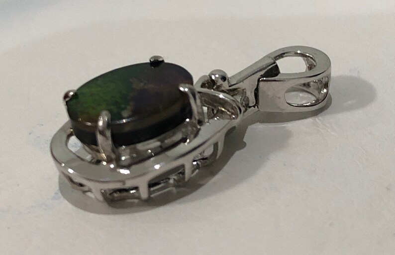 May include: Silver pendant with a black and green oval opal gemstone set in a silver frame. The pendant has a silver bail for attaching to a chain.