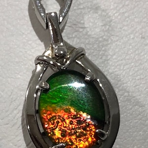 May include: A silver pendant with a green and orange iridescent gemstone. The pendant has a bail for attaching to a chain.