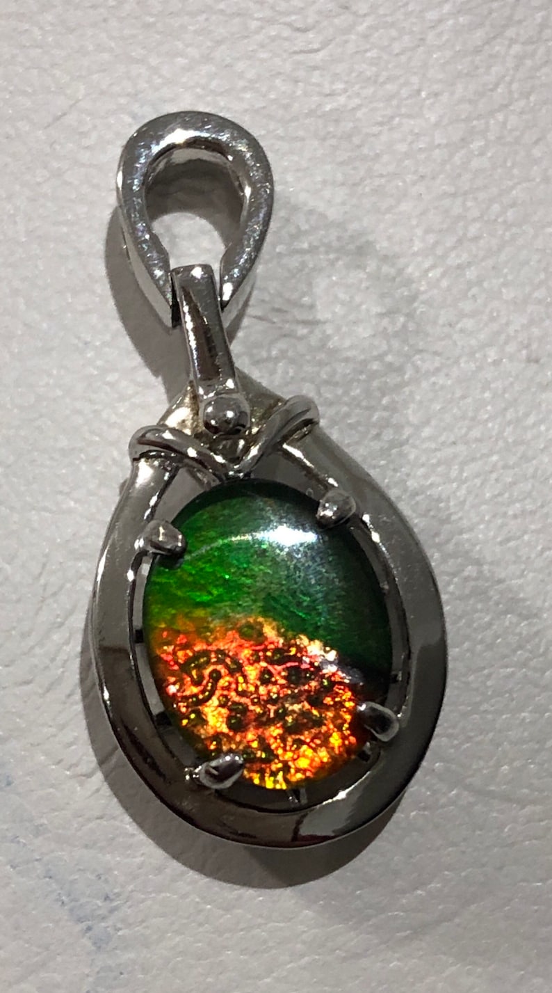 May include: A silver pendant with a green and orange iridescent gemstone. The pendant has a bail for attaching to a chain.