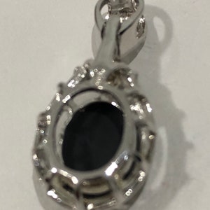 May include: A silver pendant with a black oval gemstone surrounded by a halo of smaller stones. The pendant has a bail for attaching to a chain.