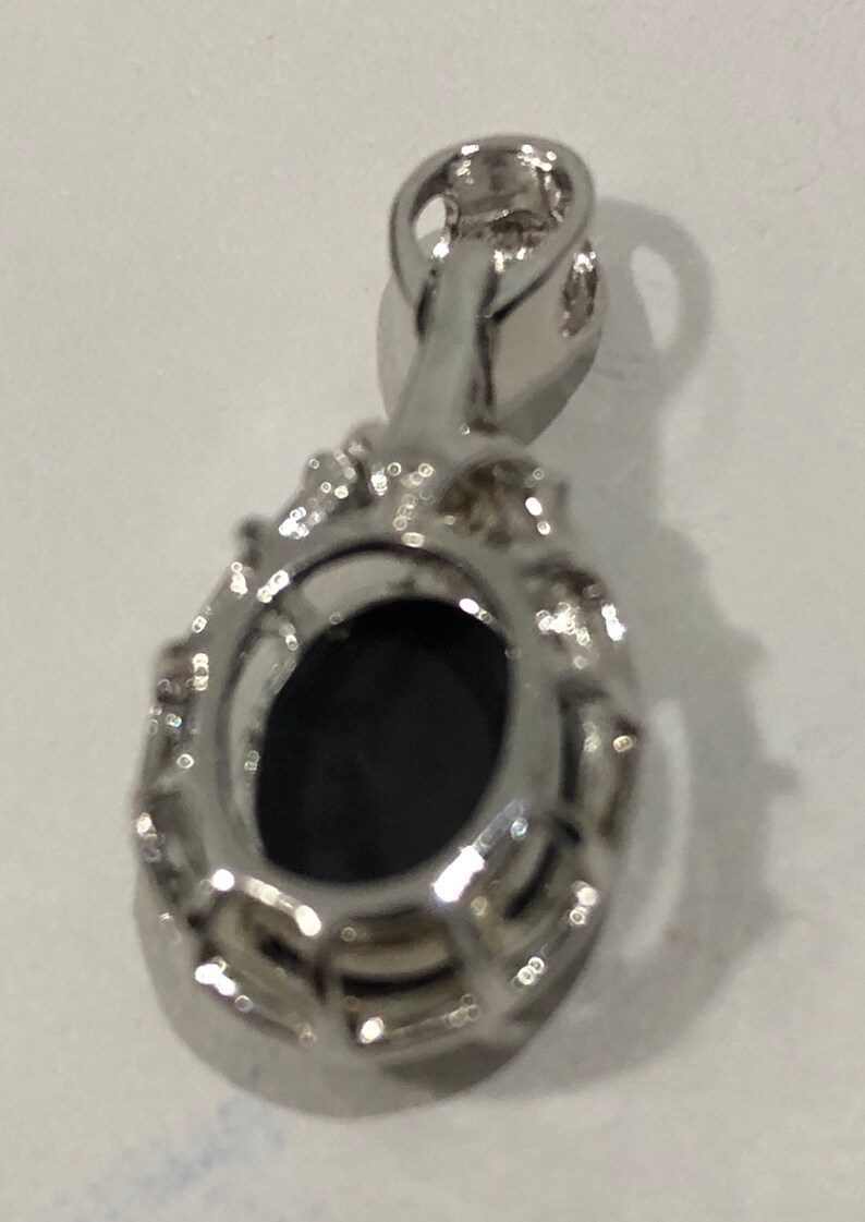 May include: A silver pendant with a black oval gemstone surrounded by a halo of smaller stones. The pendant has a bail for attaching to a chain.