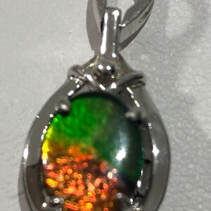 May include: A silver pendant with a green and orange iridescent gemstone. The pendant has a bail for attaching to a chain.
