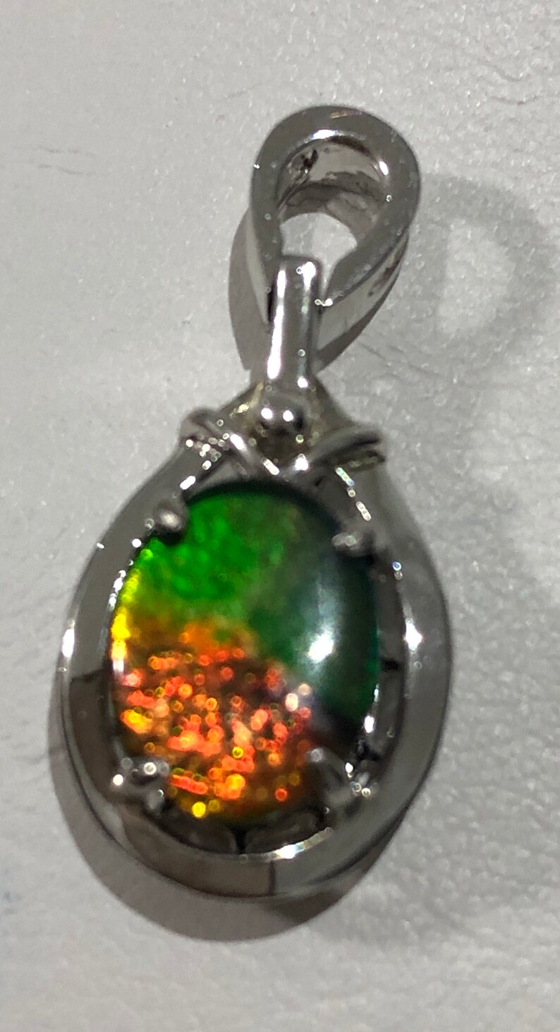 May include: A silver pendant with a green and orange iridescent gemstone. The pendant has a bail for attaching to a chain.