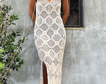May include: A woman wearing a white crochet maxi dress with a side slit. The dress has a square pattern and is sleeveless. She is wearing sunglasses and standing in front of a brick wall.