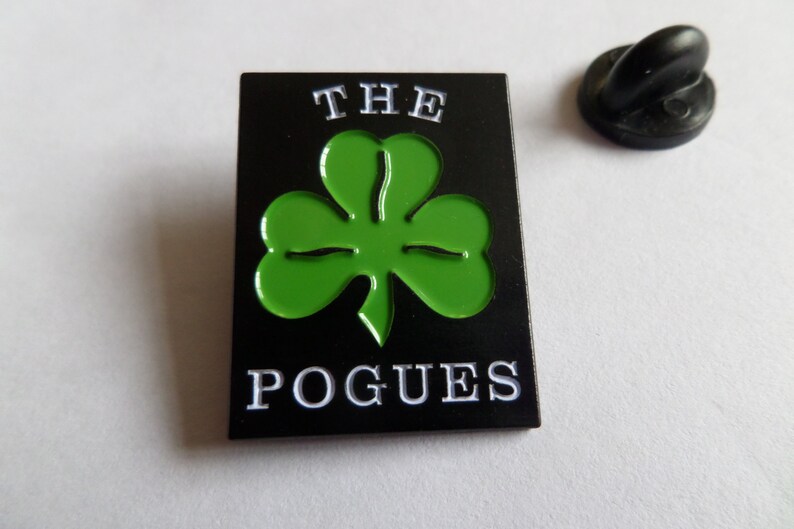 May include: Black and green enamel pin with a shamrock and the text "THE POGUES" in white.
