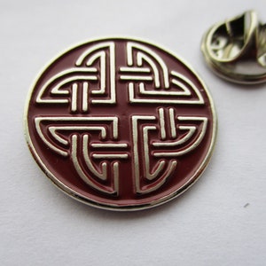 May include: A red and silver metal pin with a Celtic knot design. The pin has a safety clasp on the back.