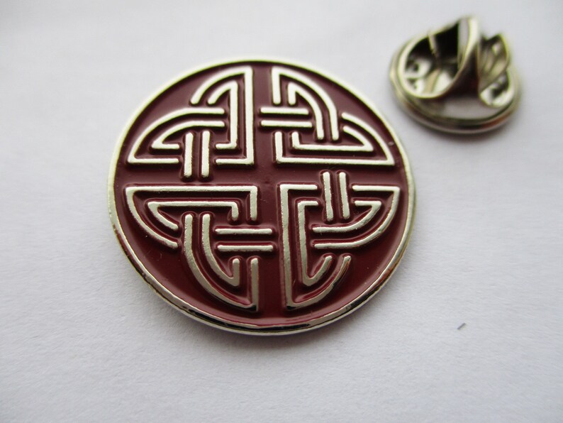 May include: A red and silver metal pin with a Celtic knot design. The pin has a safety clasp on the back.