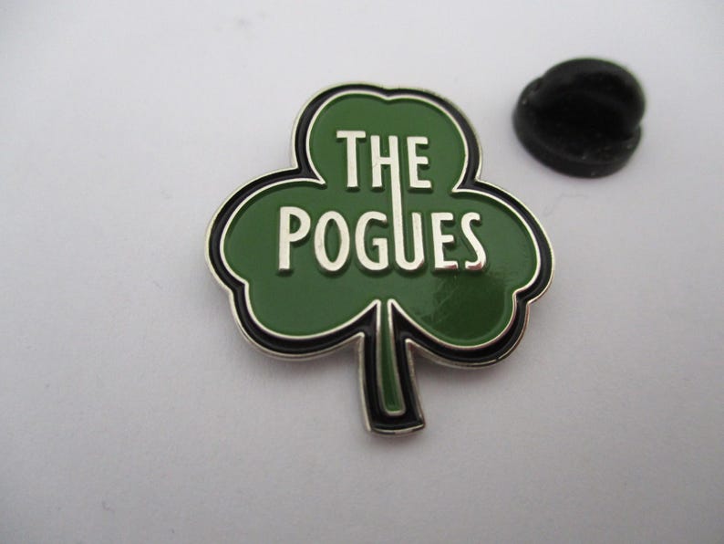 May include: A green shamrock-shaped pin with a silver border and the text "THE POGUES" in white letters.